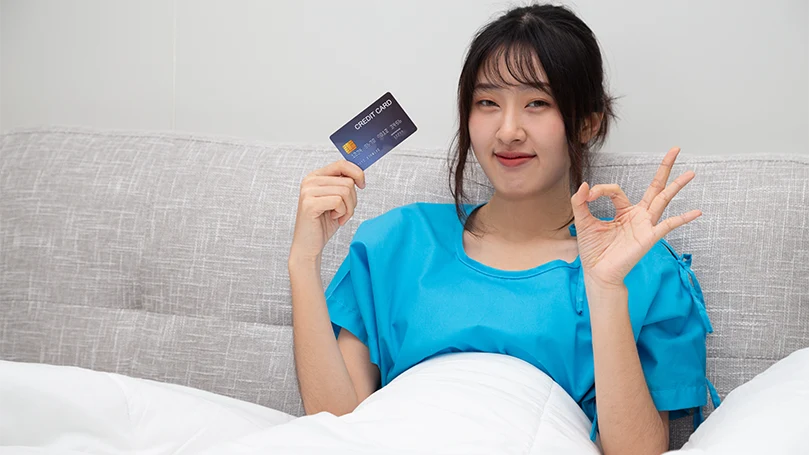 Eine asiatische Frau im Bett, die ihre Kreditkarte hält