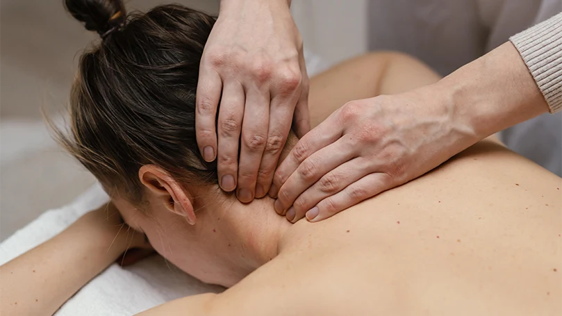Das Bild eines Therapeuten, der den Nacken einer Frau massiert.